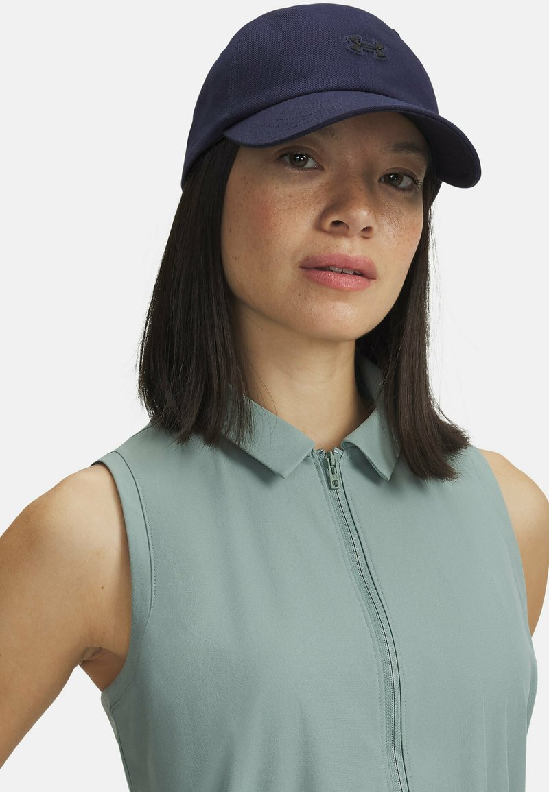Casquette bleu marine avec une visière incurvée et un logo à l'avant, associée à un haut sans manches vert clair avec une fermeture éclair à l'avant et un col.