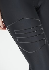 Zwarte sportleggingen met een soepele textuur, met een glanzend grijs geometrisch patroon op de dij. Close-up van de stof en ontwerpdetails.