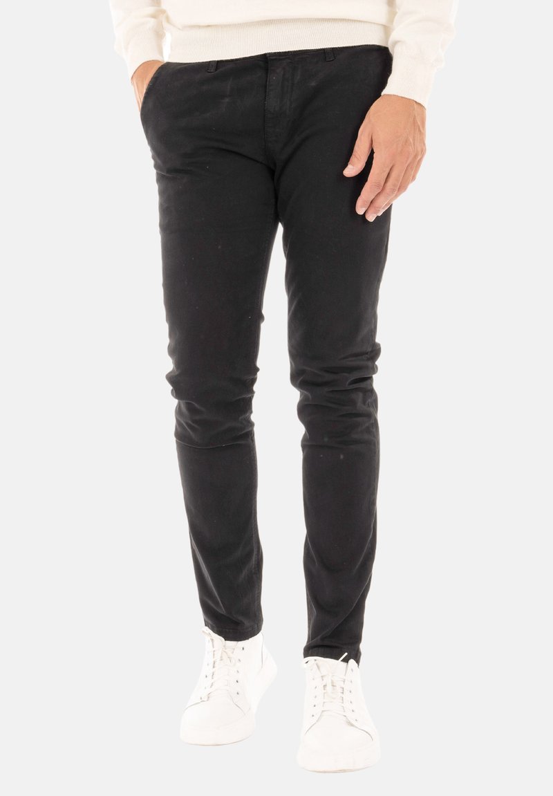 Pantaloni neri in cotone con una vestibilità slim, caratterizzati da una superficie liscia e discrete tasche frontali, abbinati a sneakers bianche.