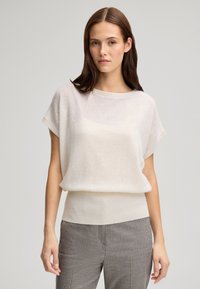 Helles beige Kurzarm-Top mit geripptem Saum und weicher Textur, kombiniert mit grau karierter Hose, die eine lässige Silhouette schafft.