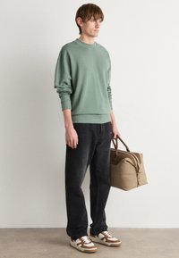 Sudadera de algodón verde, pantalones vaqueros negros, zapatillas marrones y crema, bolsa de mano beige con acentos marrones, ajuste casual, marca mínima y diseño relajado.
