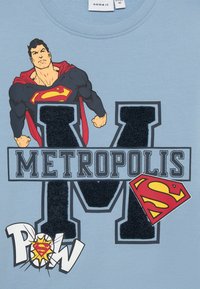 Hellblaues T-Shirt mit Superman-Grafik, dem Text "METROPOLIS", einem geprägten "M" und einem comic-artigen "POW"-Detail. Aus Baumwolle.