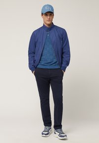 Giacca bomber blu navy, maglione blu a trama, pantaloni navy e sneaker blu con dettagli bianchi. Berretto blu con ricami.