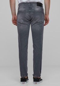 Grå denimjeans med rett snitt, fem lommer og en lett falmet tekstur. Slitte sømmer. Stylet med svarte sko.