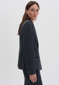 Blazer su misura grigio scuro realizzato in un tessuto liscio. Presenta maniche lunghe, collo a rever e chiusura con un solo bottone. Design semplice.