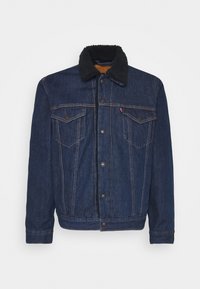 Denim jacket featuring a dark blue wash, black sherpa collar, two chest pockets, metal buttons, and contrast stitching.