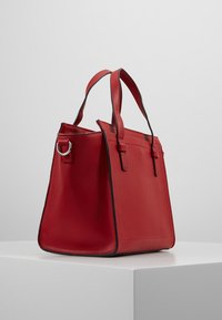 Rote Lederhandtasche mit strukturiertem Format, doppelten Griffen und kontrastierender schwarzer Paspelierung. Verfügt über einen Metallschlaufenakzent auf einer Seite.