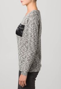 Stickad grå pullover med en svart satinlapp fram, med rundad halsringning och långa ärmar. Strukturerad tyg med en avslappnad passform.