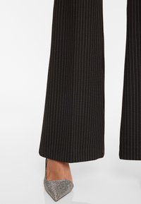 Zwart, op maat gemaakte broek met witte streepjes, met een wijd been ontwerp. Gepaard met een puntige, metallic zilveren hoge hak.