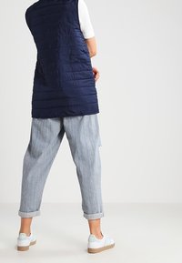 Marinblå puffer-väst med horisontell sömnad, tillsammans med ljusblå randiga byxor och vita sneakers med ljusa detaljer och beige sulor.