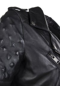 Giacca di pelle nera con una texture liscia e spalle testurizzate con borchie a piramide. Include una chiusura con zip e dettagli con collo a scatto.