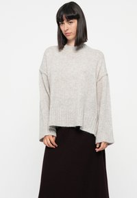 Light gray knitted sweater with a ribbed hem, oversized fit, and dropped shoulders. Worn over a dark brown skirt.