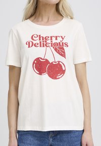 T-shirt en coton crème à manches courtes, col rond, avec un graphisme rouge de deux cerises et le texte "Cherry Delicious" au-dessus.