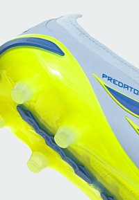 Gros plan sur la semelle d'une chaussure de football grise et jaune néon avec des crampons translucides et le logo "Predator".