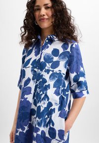 Button-up shirt in linen blend, featuring a blue and white leaf pattern, short rolled sleeves, and a front pocket. Smooth texture.