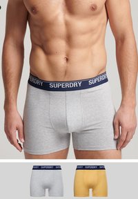 Grijze katoenen boxershorts met een marineblauwe "SUPERDRY" tailleband. Bevat afbeeldingen van lichtgrijze en gele boxers hieronder.