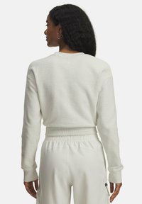 Pull blanc texturé avec un col rond et des manches longues, présentant un design court et un ourlet côtelé, associé à un pantalon de couleur claire.