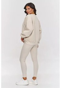 Beżowy, oversize'owy sweatshirt z opadającymi ramionami, w połączeniu z żeberkowymi, beżowymi legginsami. Model nosi białe, masywne sneakersy. Gładka tekstura.