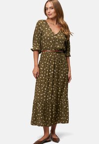 Olivgrünes Kleid mit weißen und gelben Blumenmustern, V-Ausschnitt, kurzen Ärmeln, elastischem Taillenbund und gestuftem Rock. Brauner Gürtel und Schuhe.
