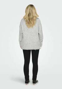 Szary sweter z dzianiny o luźnym, swobodnym kroju, z prążkowanym dołem i długimi rękawami, w połączeniu z czarnymi spodniami o slim fit i czarnymi trampkami.