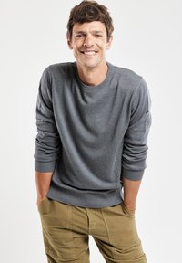 Maglione grigio a girocollo realizzato in morbido materiale a maglia, con polsini e orlo a coste. Indossato con pantaloni cargo verde oliva, senza loghi visibili.