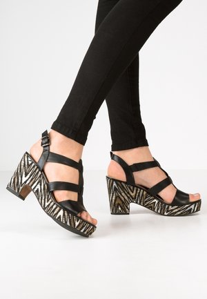 Schwarze Platform-Sandalen mit mehreren Riemen, ausgestattet mit einem gemusterten Wedge-Absatz in Schwarz, Weiß und Beige, der geometrische Designs zeigt.