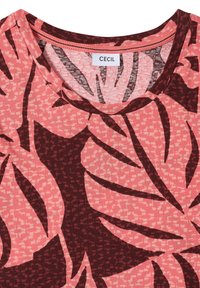T-shirt rose et bordeaux à col rond avec grand imprimé de feuilles tropicales et petit motif texturé, étiquette avec "CECIL" visible à l'intérieur du col.