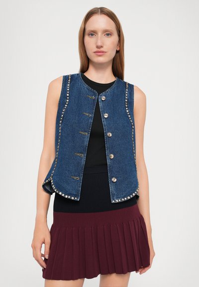 Denim vests ar pieguļošu dizainu, bronzas pogām, dekoratīviem kniedēm gar malām un nedaudz izplešamu apakšmalu. Apvienots ar ribotu melnu topu.