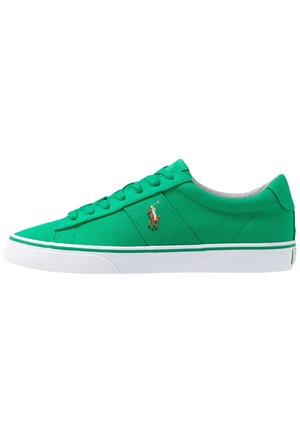 Zapatilla baja de lona verde con suela blanca, una raya verde, cordones y un pequeño logo bordado de jugador de polo en el lateral.