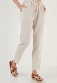 Beige elastische taillebroek met zijzakken en een relaxte pasvorm. Gecombineerd met bruine espadrillesandalen met geweven accenten.