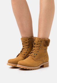 Bottines en suède beige avec un col en fourrure rembourré, des œillets en métal et une semelle en caoutchouc. Comprend des lacets et des détails de surpiqûre sur les côtés.