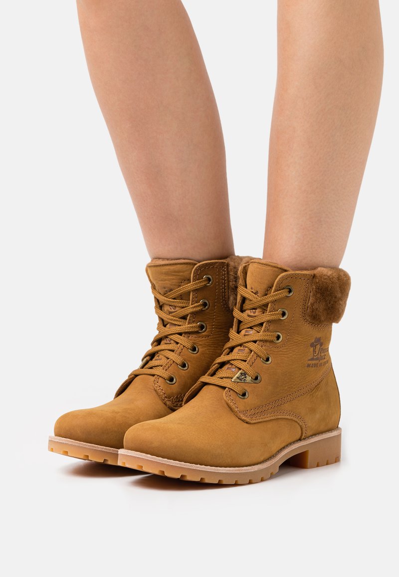 Bottines en suède beige avec un col en fourrure rembourré, des œillets en métal et une semelle en caoutchouc. Comprend des lacets et des détails de surpiqûre sur les côtés.