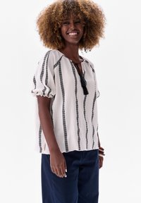 Witte blouse met zwarte verticale strepen, lichte textuurstof, losse pasvorm, geplooide mouwen en een kwastje detail bij de halslijn.