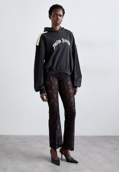 Black oversized hoodie with "Palm Angels" logo, paired with black lace flared pants, and pointed-toe heels on a neutral background.