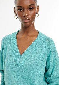 Turquoise knit sweater with a v-neckline, ribbed cuffs, and relaxed fit. Soft texture with subtle variations in color throughout.