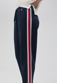 Mornarska trenirka s elastičnim pojasom i vezicom, s krem, crvenim i plavim bočnim trakama. Mekana tkanina s opuštenim krojem.