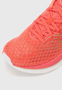 Zapatilla de correr de malla color coral con una parte superior texturizada, acento de logo dorado y una suela de goma blanca con un diseño de punta redondeada.