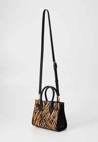 Tan og svart tigerstripete håndveske med en strukturert design, utstyrt med doble håndtak og en avtakbar skulderrem. Glatt tekstur.