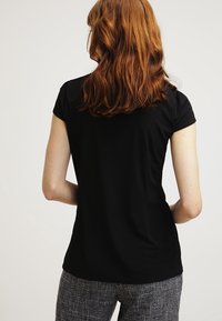 Svart kortärmad blus med en jämn textur, med en rundad halsringning. Plagget är figursytt och visas från baksidan med en avslappnad silhuett.