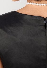 Abito in tessuto nero con una trama liscia, dotato di chiusura con zip sul retro. Accentuato da una collana di perle intorno allo scollo.