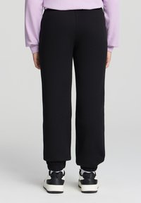 Czarne dresy z prostymi nogawkami, elastycznymi mankietami i gładką teksturą, w połączeniu z czarno-białymi sneakersami.