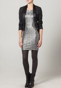 Silvrig paljettklänning med en figurnära silhuett, tillsammans med en svart satinblazer, mörkgrå strumpbyxor och svarta ankelstövlar.