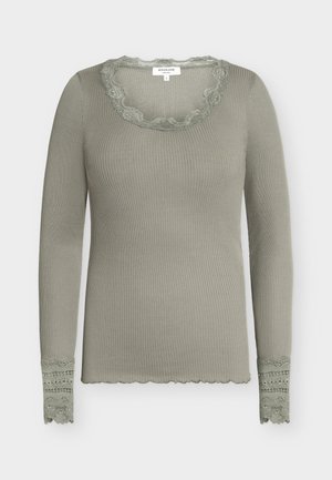 Kerge oliivrohelise varjundiga soonikkoes pikkade varrukatega pluus pitsist ääristega kaardus V-kaelusel ja varrukaotstel, liibuv siluett ning serva diagonaalne laineline äär.