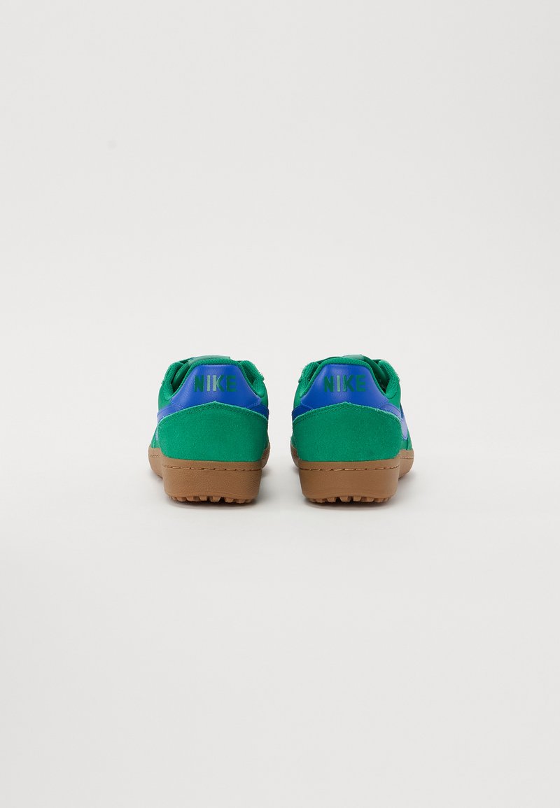 Sneaker in camoscio verde con accenti blu, dotate di suola in gomma marrone. La parte posteriore mostra il logo NIKE in verde. Design con lacci piatti.