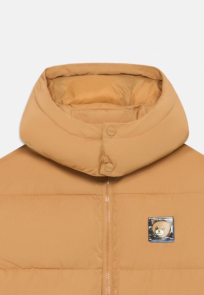 Tanskleurige pufferjack met hoge kraag, voorrits en geborduurd berenpatch. Glad, glanzend materiaal met gestikte secties.