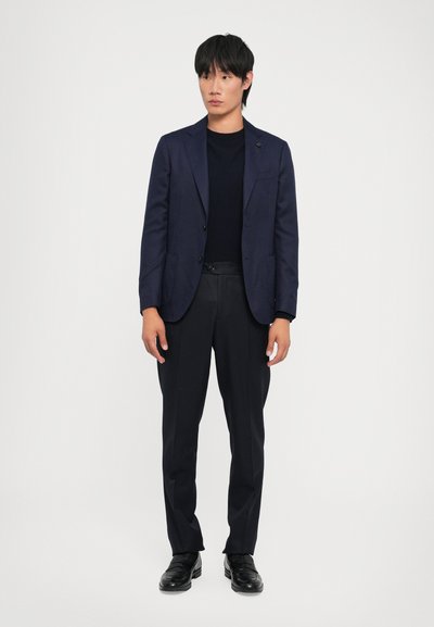 Navy blazer with two buttons, slim fit, worn over a black crewneck sweater. Paired with tailored black trousers and black dress shoes.
