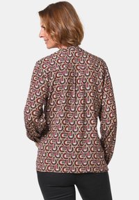 Musterbluse mit langen Ärmeln, die Kreise und Streifen in Brauntönen, Rosa und Creme zeigt; leichter Stoff mit lockerer Passform.