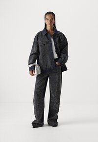 Chaqueta de mezclilla y pantalones a juego en azul oscuro con un patrón salpicado en blanco. Presenta un corte oversize, dos bolsillos frontales y cierre de botones.