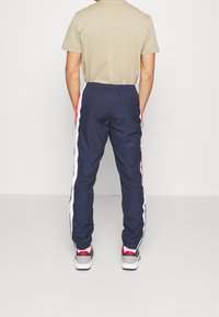 Navy träningsbyxor med vita och röda sidostråk, elastisk midja och muddar vid anklarna, tillverkade av ett jämnt, lätt material.