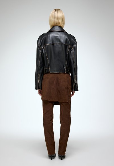 Black leather cropped jacket with visible stitching, paired with brown suede trousers. The outfit has a fitted silhouette and zip details.